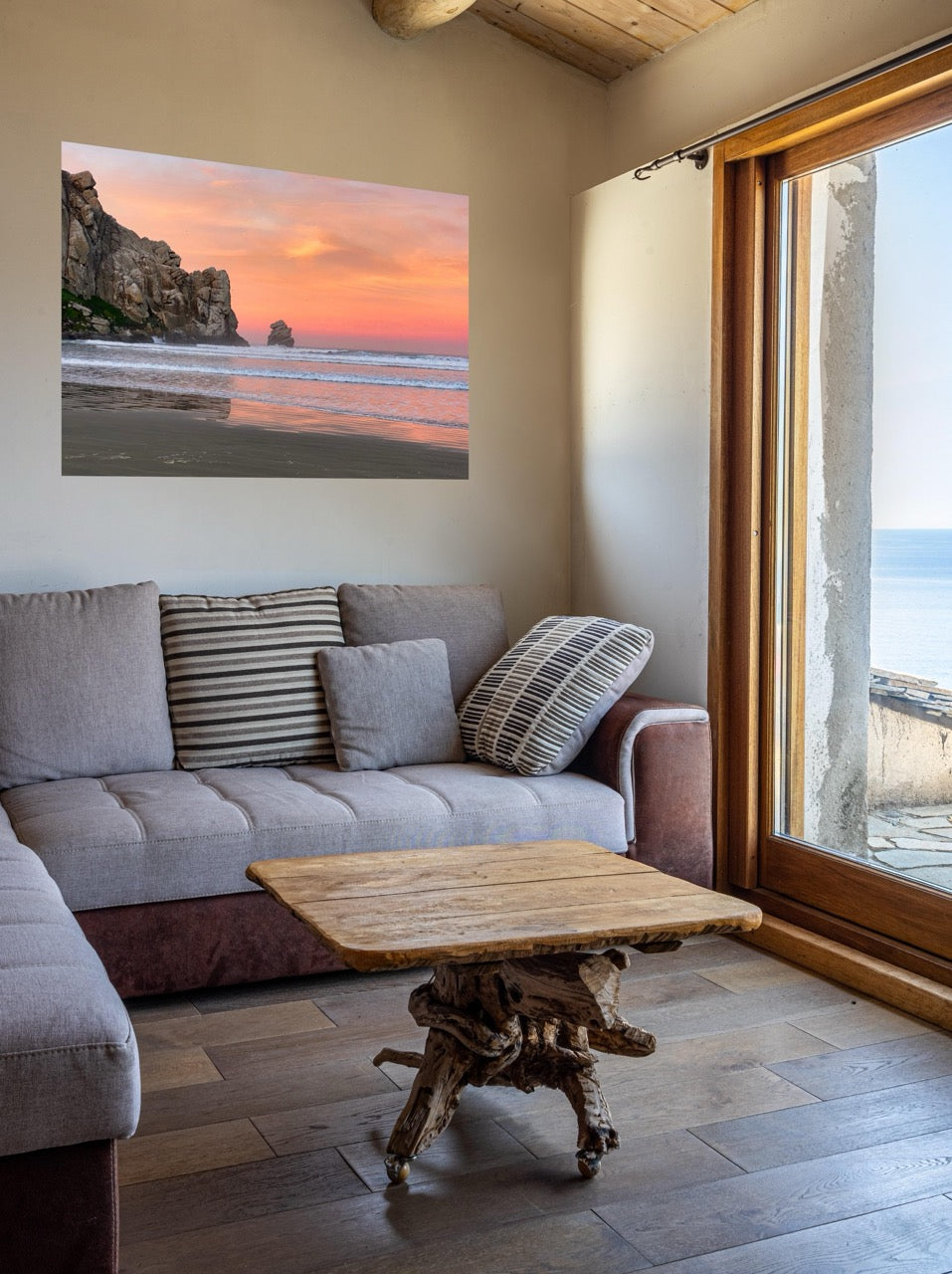 Living room with a gray sofa, wooden coffee table, and a large window showing a beach view.