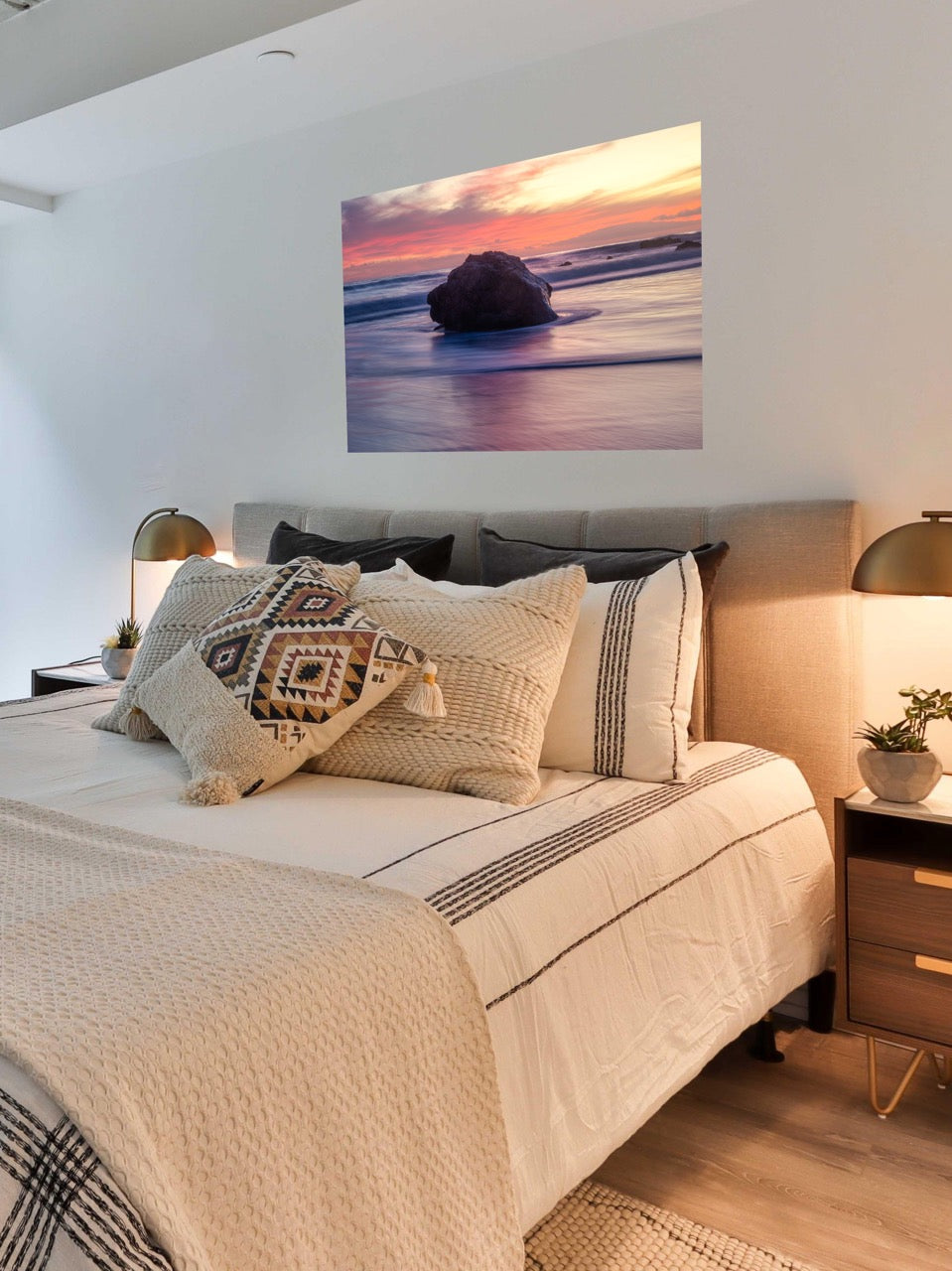 Bedroom with a bed featuring patterned pillows and a canvas print of a large ocean rock on the wall.