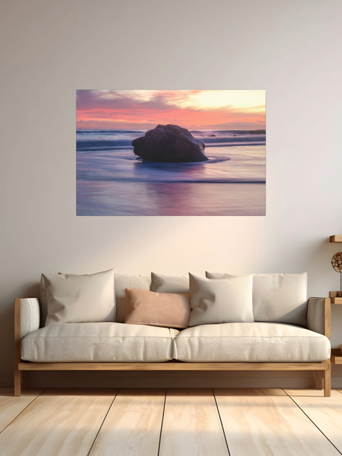A canvas print of a large ocean rock on a wall above a sofa with cushions.