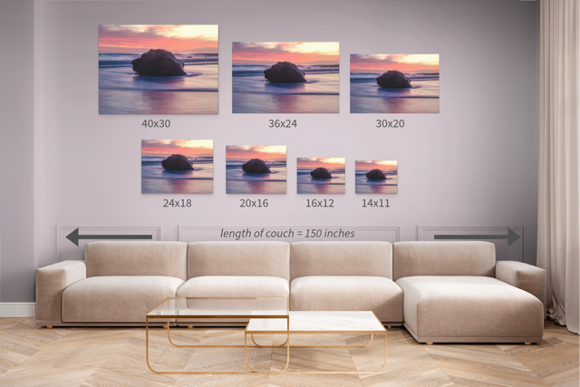 A canvas print of a large ocean rock displayed in seven different sizes above a beige sofa.
