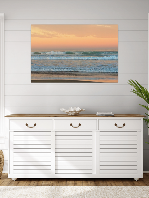 White cabinet with wooden top against a wall with a canvas print of a sunrise sky over ocean waves.