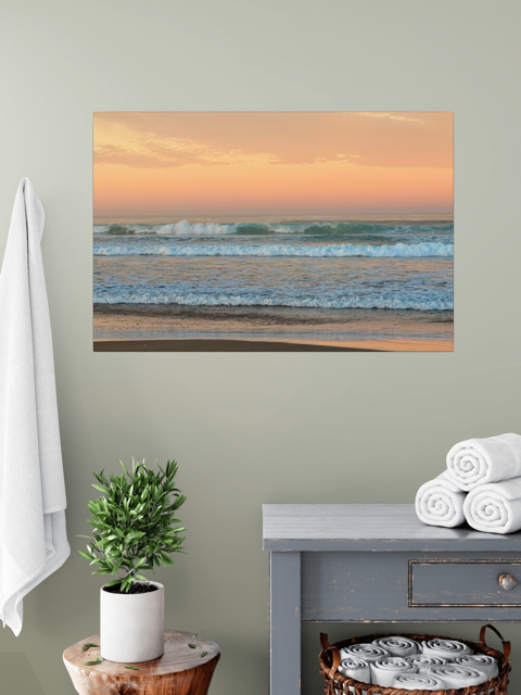 Canvas print of a sunrise sky over ocean waves on a wall above a plant and towels