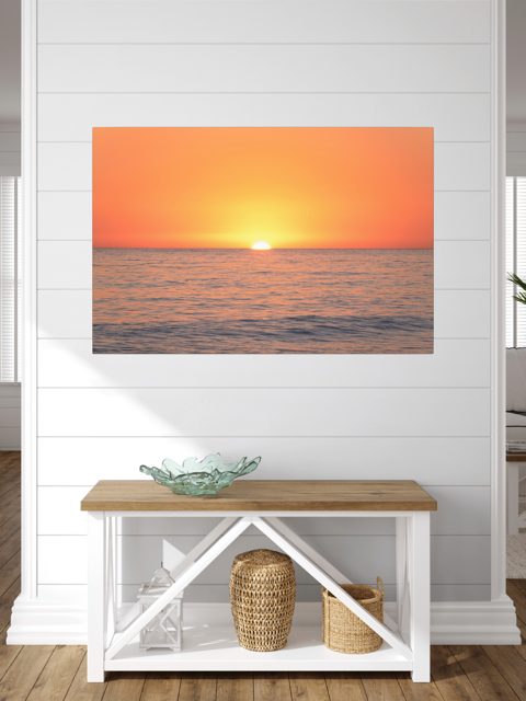 A canvas print of a sunset over the ocean on the wall above a bench.