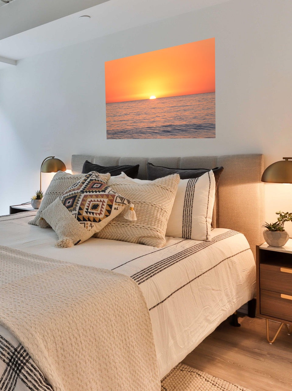 Bedroom with a canvas print of a sunset over the ocean on the wall above the bed.