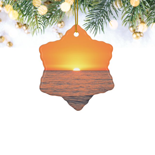 Ceramic Christmas ornament featuring a minimalist photograph of a vibrant orange and amber sunset sky over a calm Pacific Ocean, hanging against a festive background.