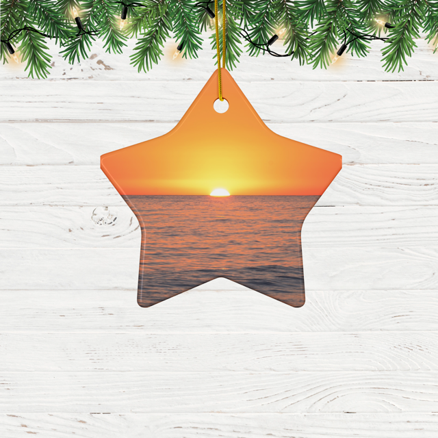Star-shaped ceramic Christmas ornament featuring a minimalist photograph of a vibrant orange and amber sunset sky over a calm Pacific Ocean hanging from a Christmas tree.