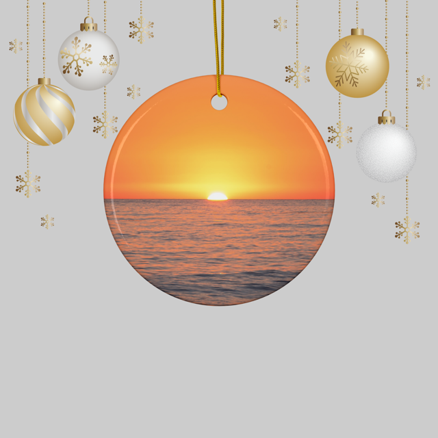 Ceramic Christmas ornament featuring a minimalist photograph of a vibrant orange and amber sunset sky over a calm Pacific Ocean, hanging against a light gray background with Christmas ornaments.