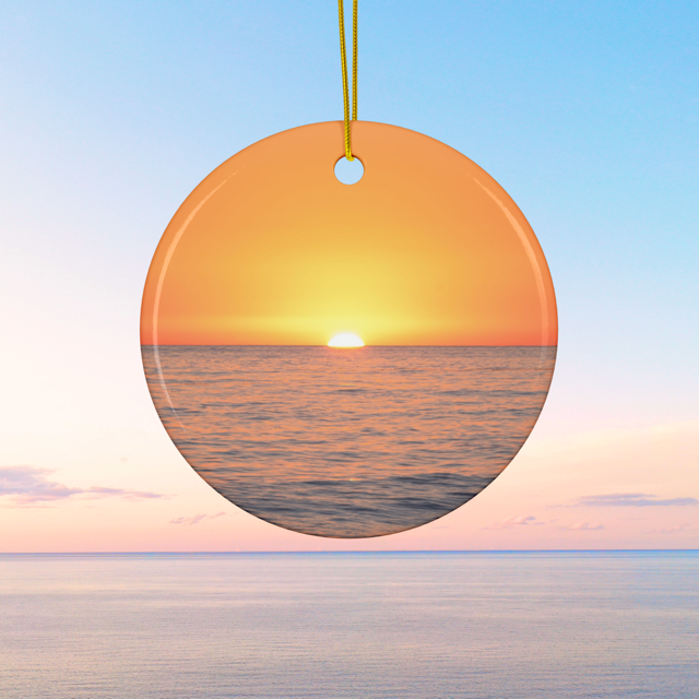 Ceramic Christmas ornament featuring a minimalist photograph of a vibrant orange and amber sunset sky over a calm Pacific Ocean on a clear blue sky background
