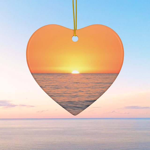 Heart-shaped ceramic Christmas ornament featuring a minimalist photograph of a vibrant orange and amber sunset sky over a calm Pacific Ocean