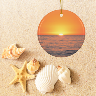 Ceramic Christmas ornament featuring a minimalist photograph of a vibrant orange and amber sunset sky over a calm Pacific Oceanon sand with shells and a starfish
