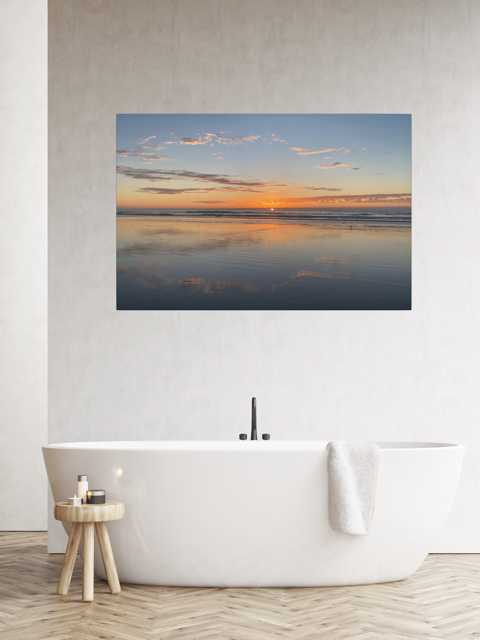 Pacific Ocean sunset reflection on beach during King Tide canvas print on a wall above a white bathtub in a bathroom.