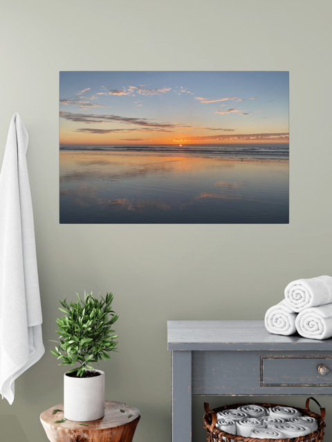 Pacific Ocean sunset reflection on beach during King Tide canvas print on a wall above a table with a plant and folded towels.