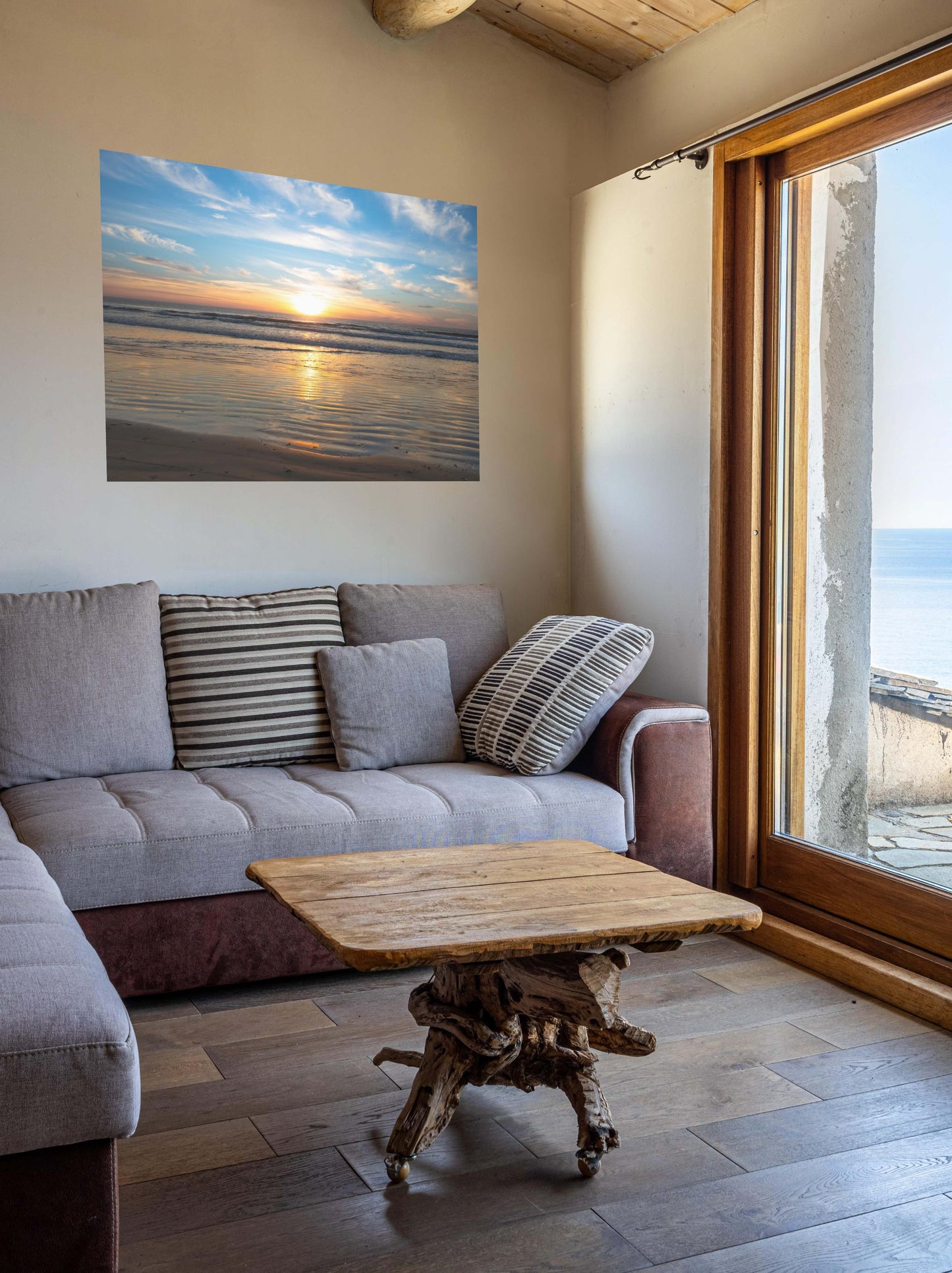Living room with a gray sofa, wooden coffee table, and a California beach sunset over the ocean with golden sand ripples canvas print.