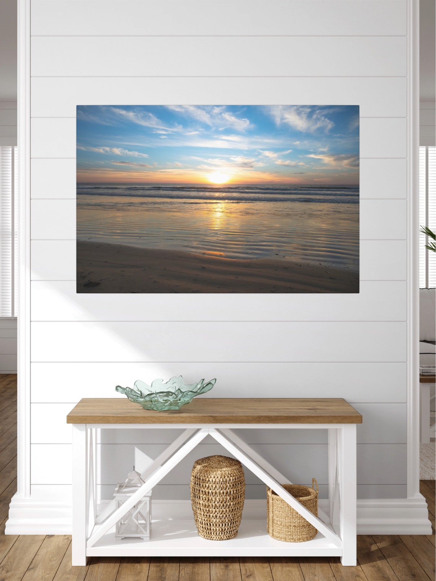 California beach sunset over the ocean with golden sand ripples canvas print on a wall above a wooden bench with a glass bowl and baskets.