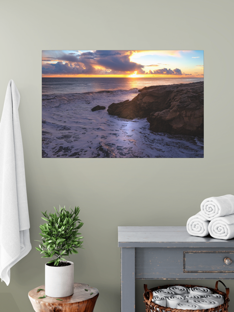 California coastal sunset after rain storm canvas print on a wall above a table with a plant and folded towels.