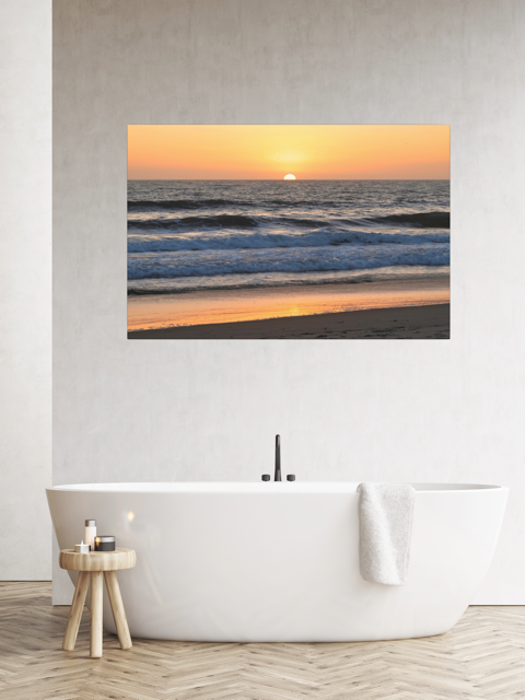 Pacific Ocean sunset and waves on beach canvas print on a wall above a bathtub in a modern bathroom.