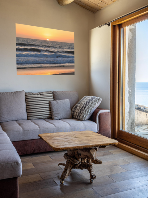 Living room with a gray sofa, wooden coffee table, and a Pacific Ocean sunset and waves on beach canvas print.