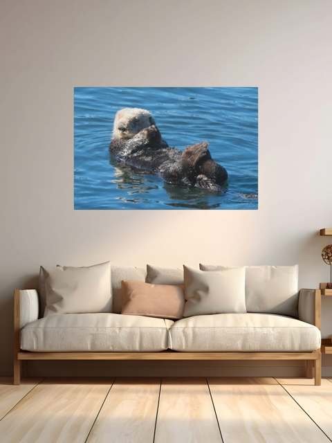 Poster of a sea otter in water on a wall above a sofa.