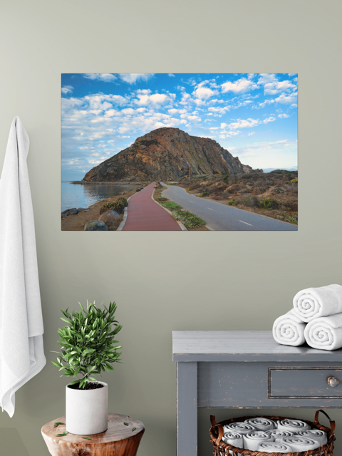 Road to Morro Rock canvas print on a gray wall above a table with towels and a plant.