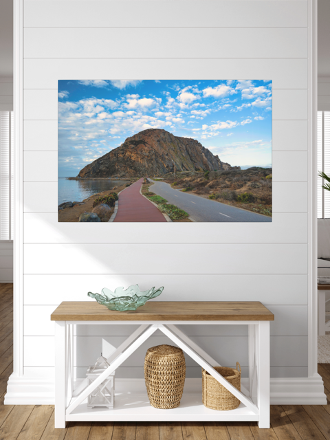 Road to Morro Rock canvas print on a white wall above a wooden bench.