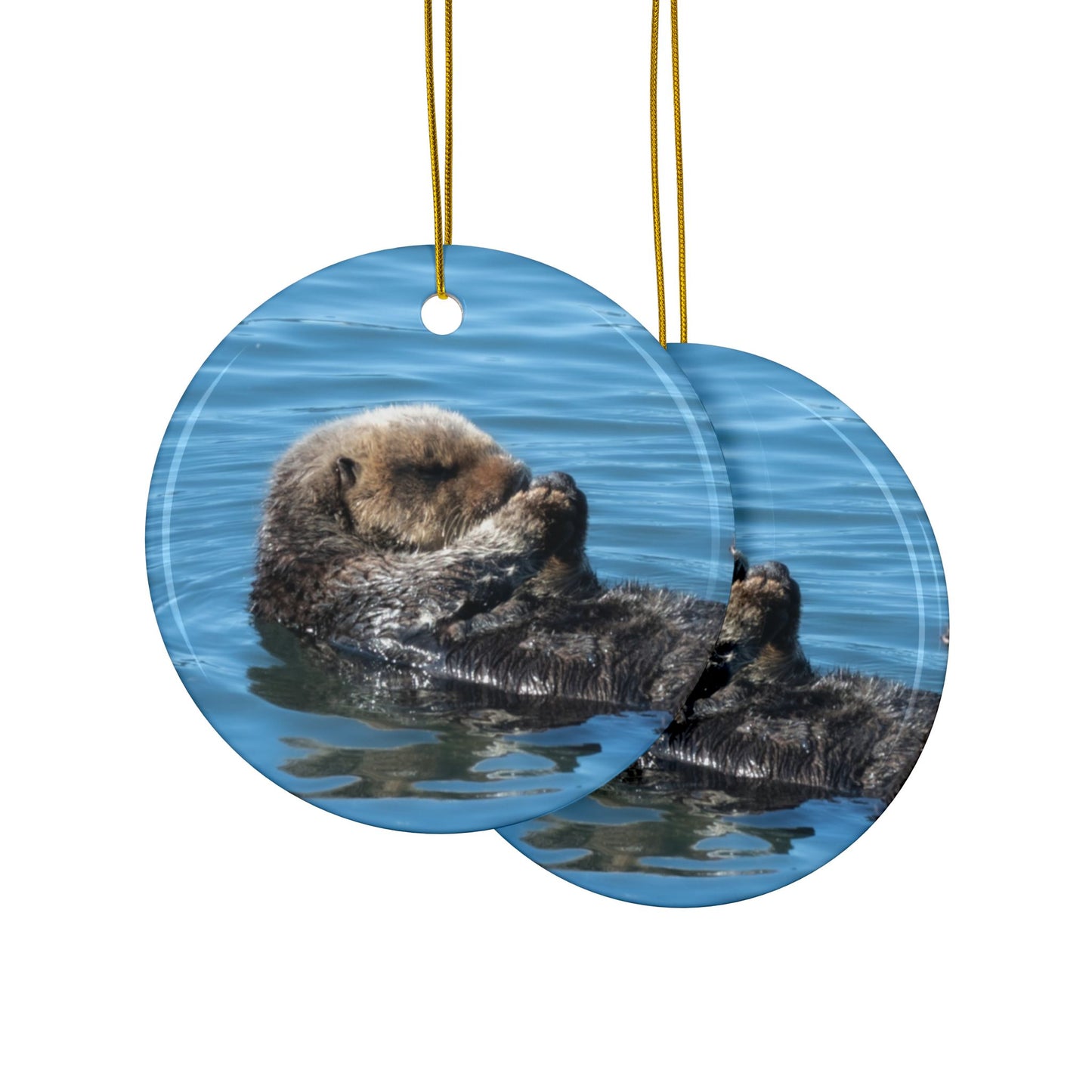 Front and back side of a ceramic Christmas ornament featuring a peaceful photograph of a sea otter with its eyes closed