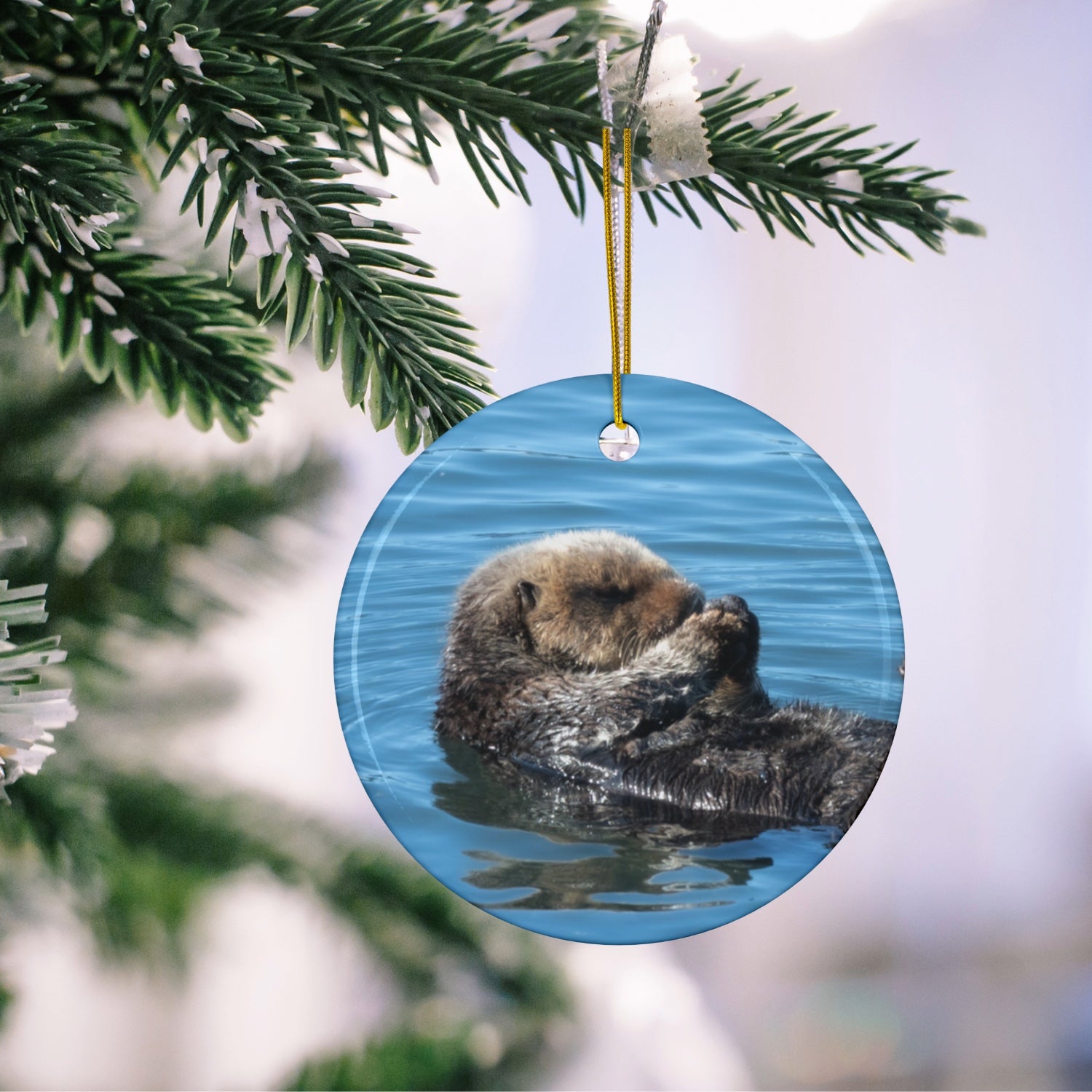 Ceramic Christmas ornament featuring a peaceful photograph of a sea otter with its eyes closed, hanging on a Christmas tree.