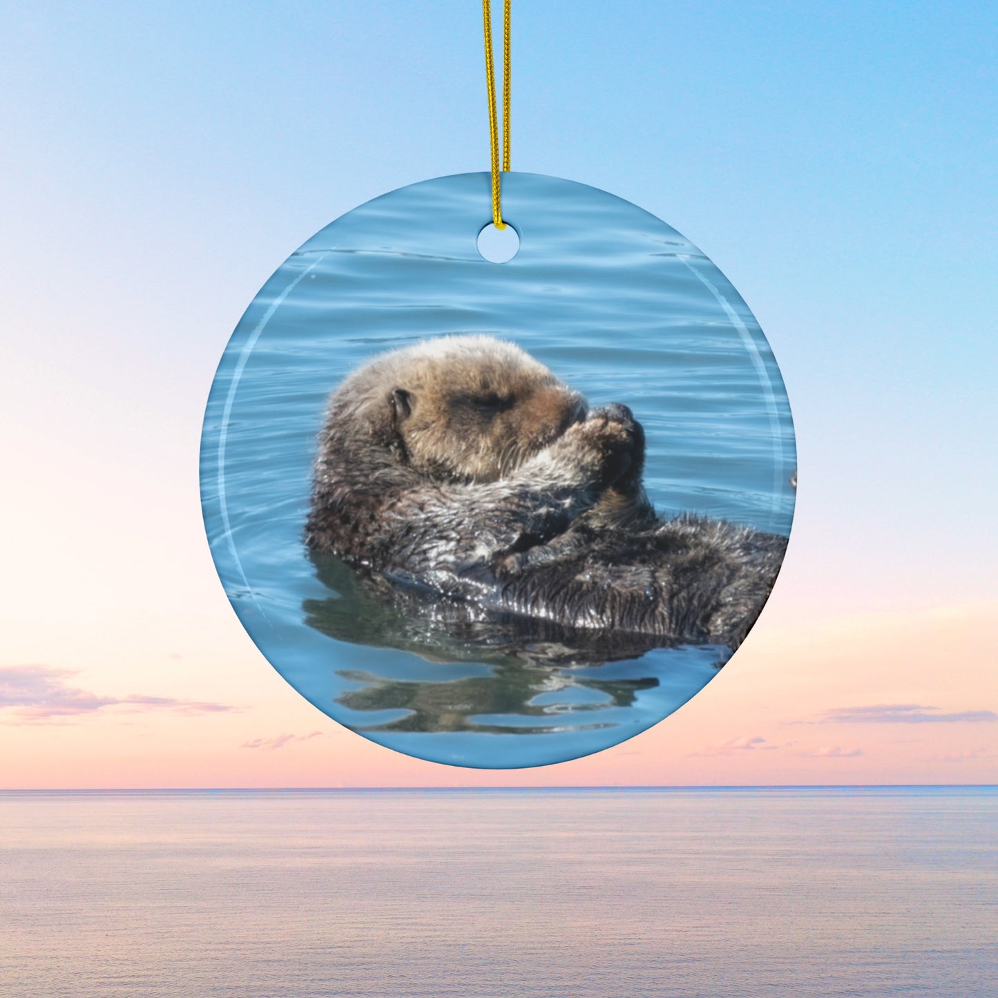 Ceramic Christmas ornament featuring a peaceful photograph of a sea otter with its eyes closed