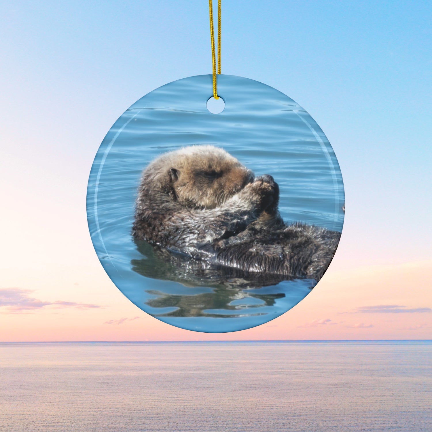 Ceramic Christmas ornament featuring a peaceful photograph of a sea otter with its eyes closed