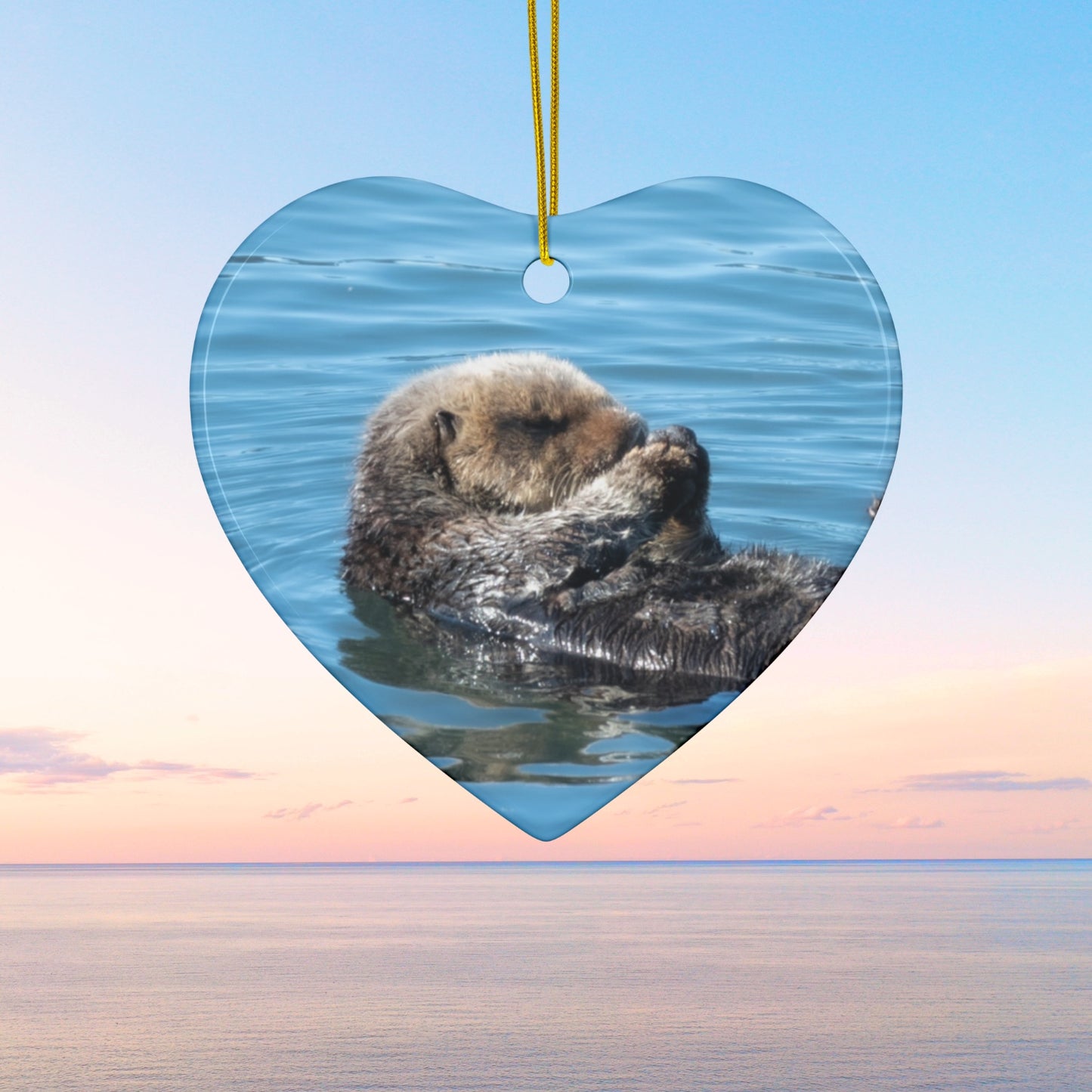 Heart-shaped ceramic Christmas ornament featuring a peaceful photograph of a sea otter with its eyes closed,