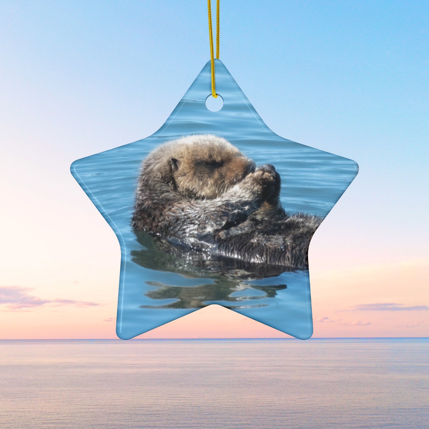 Star-shaped ceramic Christmas ornament featuring a peaceful photograph of a sea otter with its eyes closed,