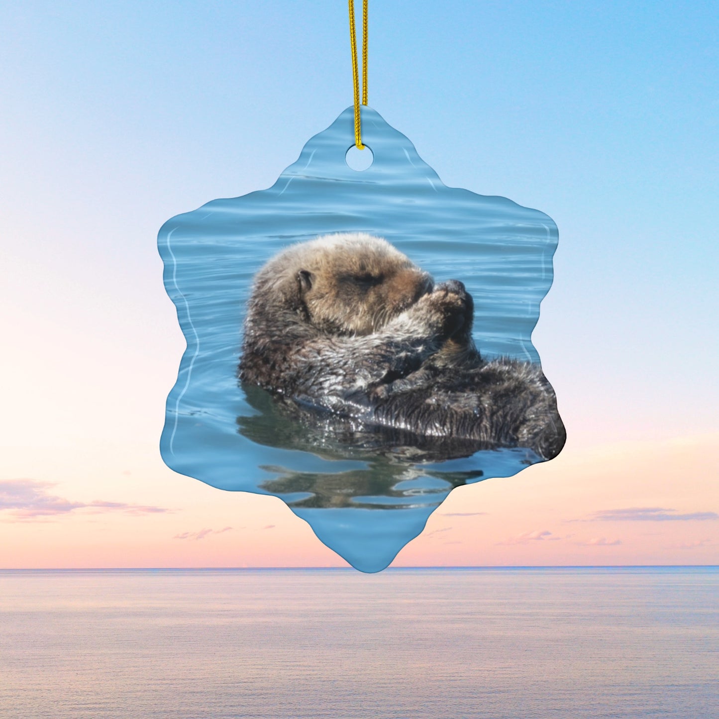 Ceramic Christmas ornament featuring a peaceful photograph of a sea otter with its eyes closed