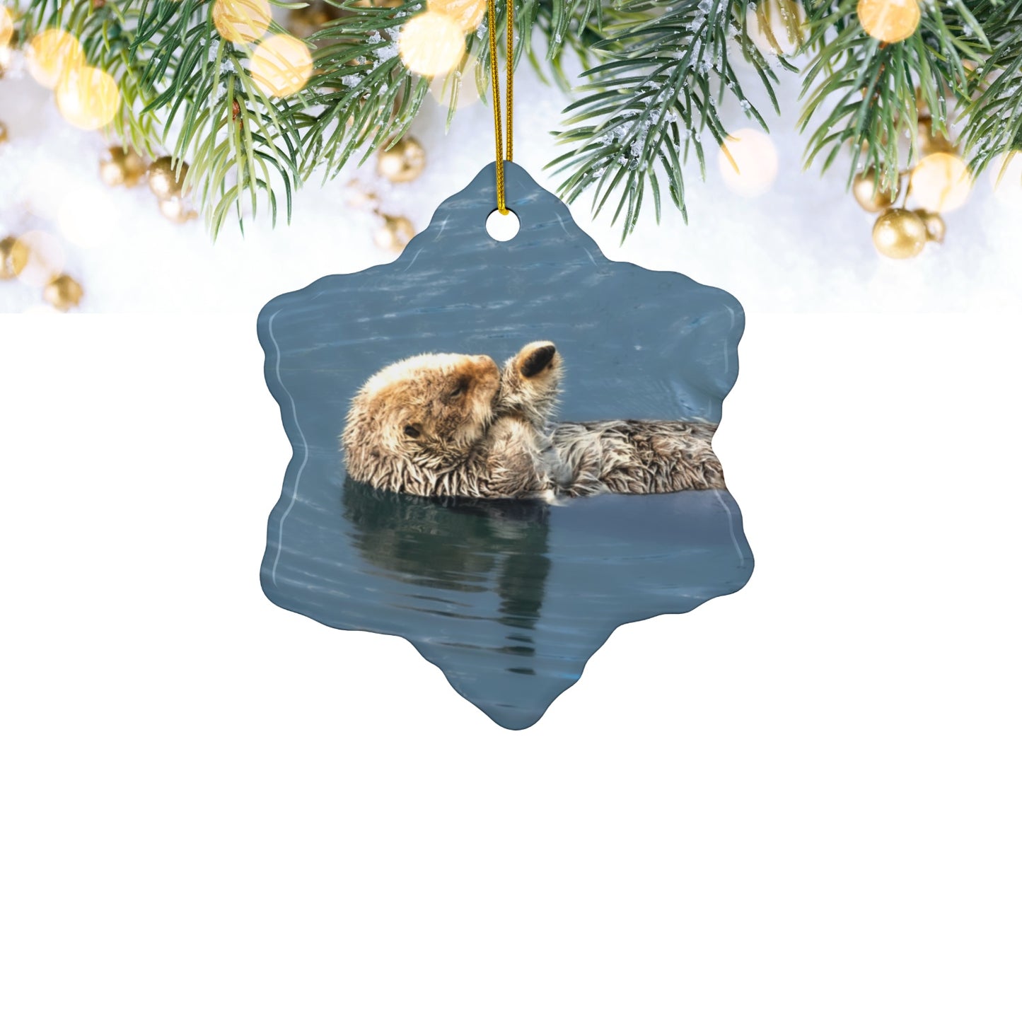 Ceramic holiday ornament featuring a professional photograph of a sea otter floating on its back in the blue waters of the Pacific Ocean hanging among Christmas lights.
