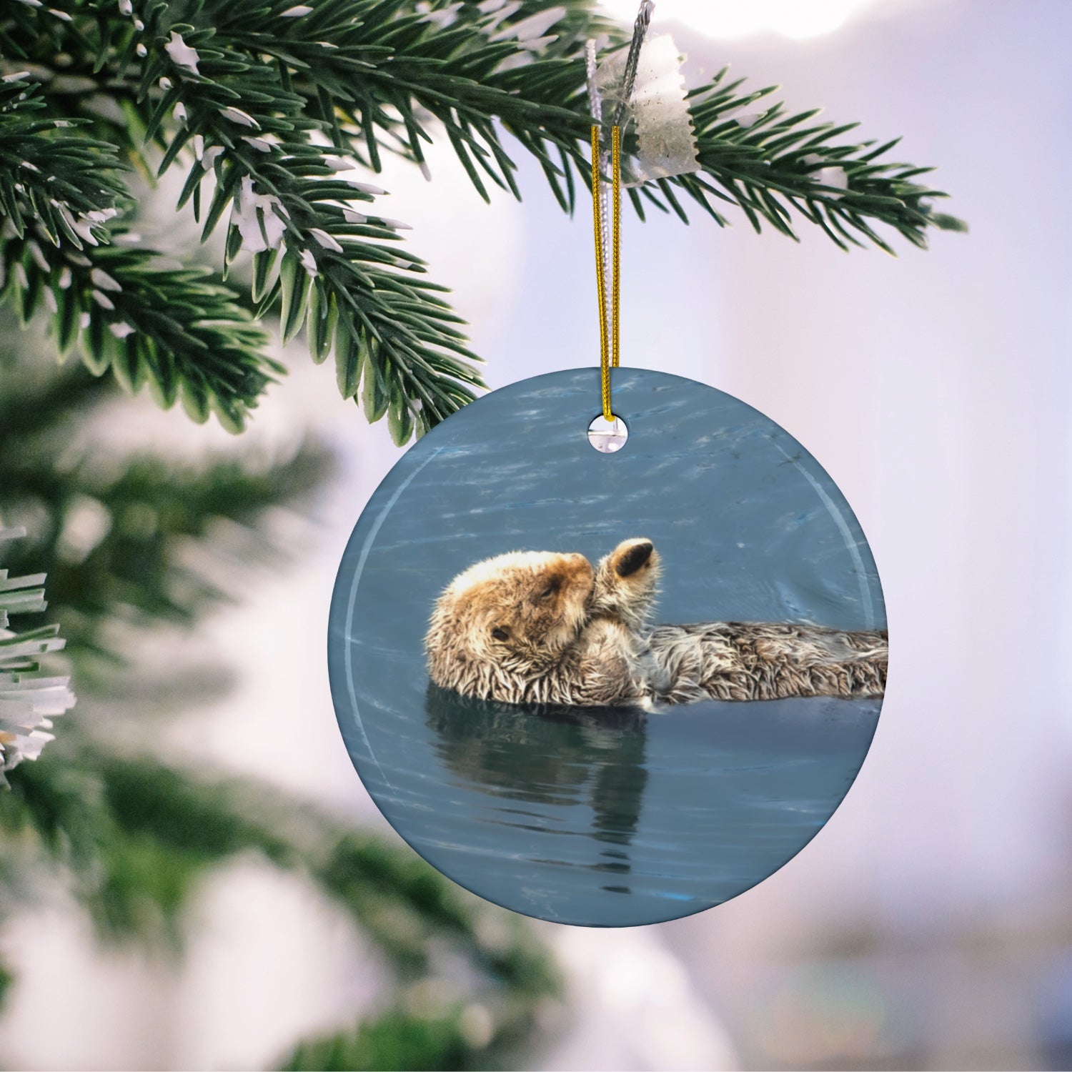 Round ornament featuring a professional photograph of a sea otter floating on its back in the blue waters of the Pacific Ocean hanging on a tree branch.