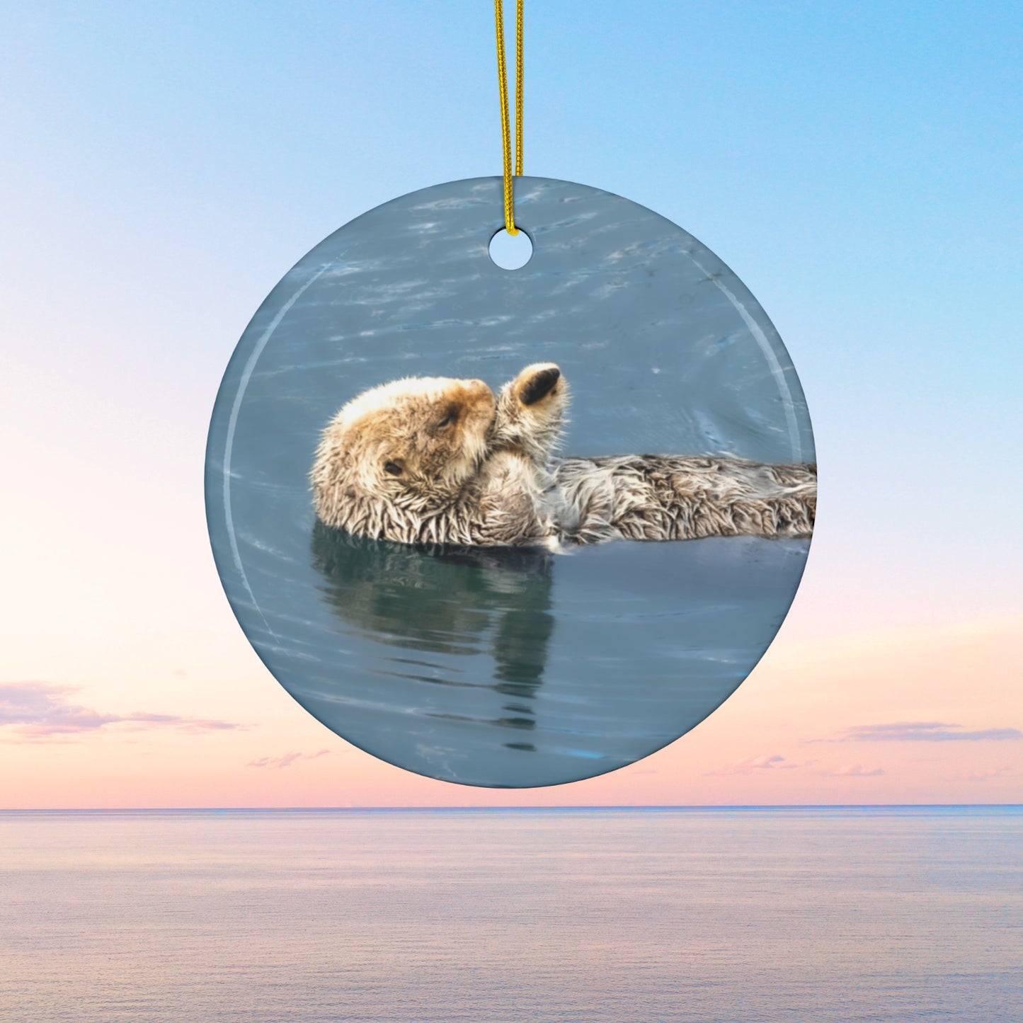 Round ornament featuring a professional photograph of a sea otter floating on its back in the blue waters of the Pacific Ocean