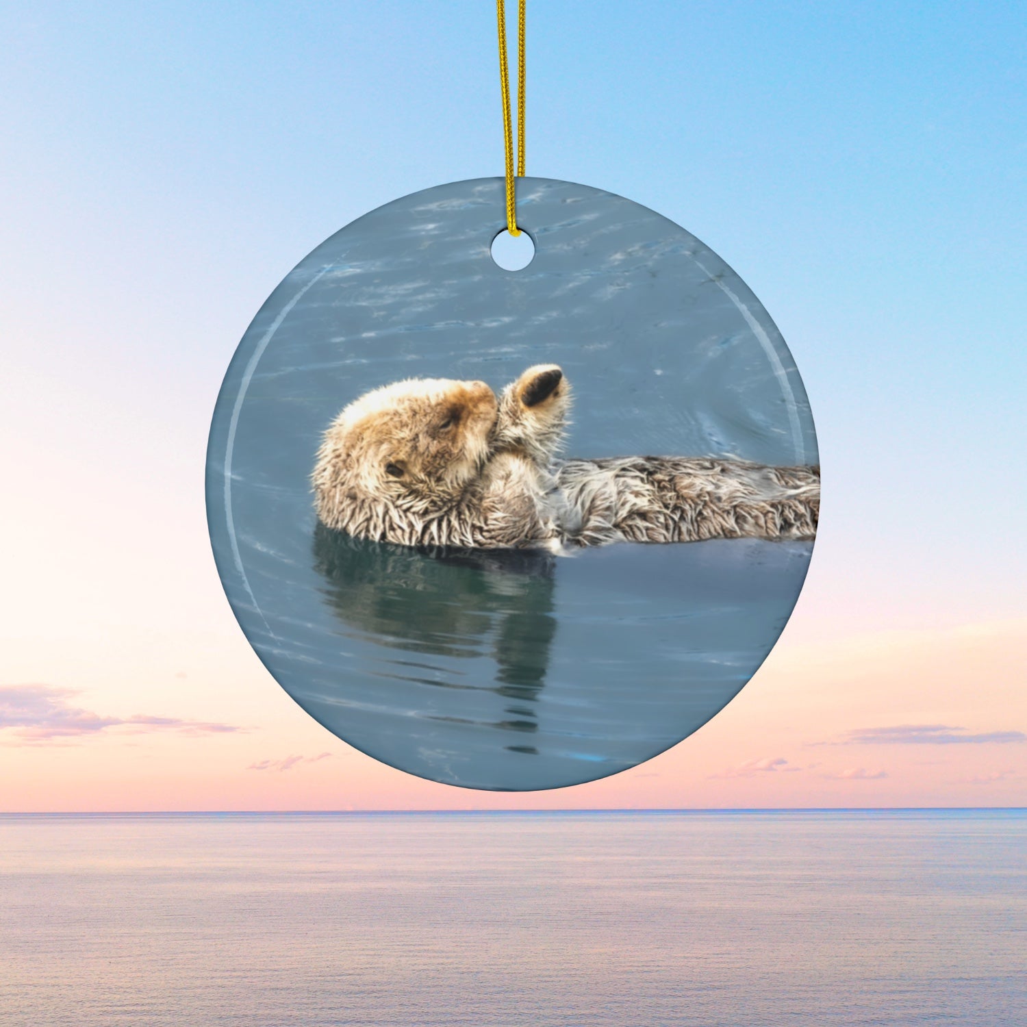 Round ornament featuring a professional photograph of a sea otter floating on its back in the blue waters of the Pacific Ocean