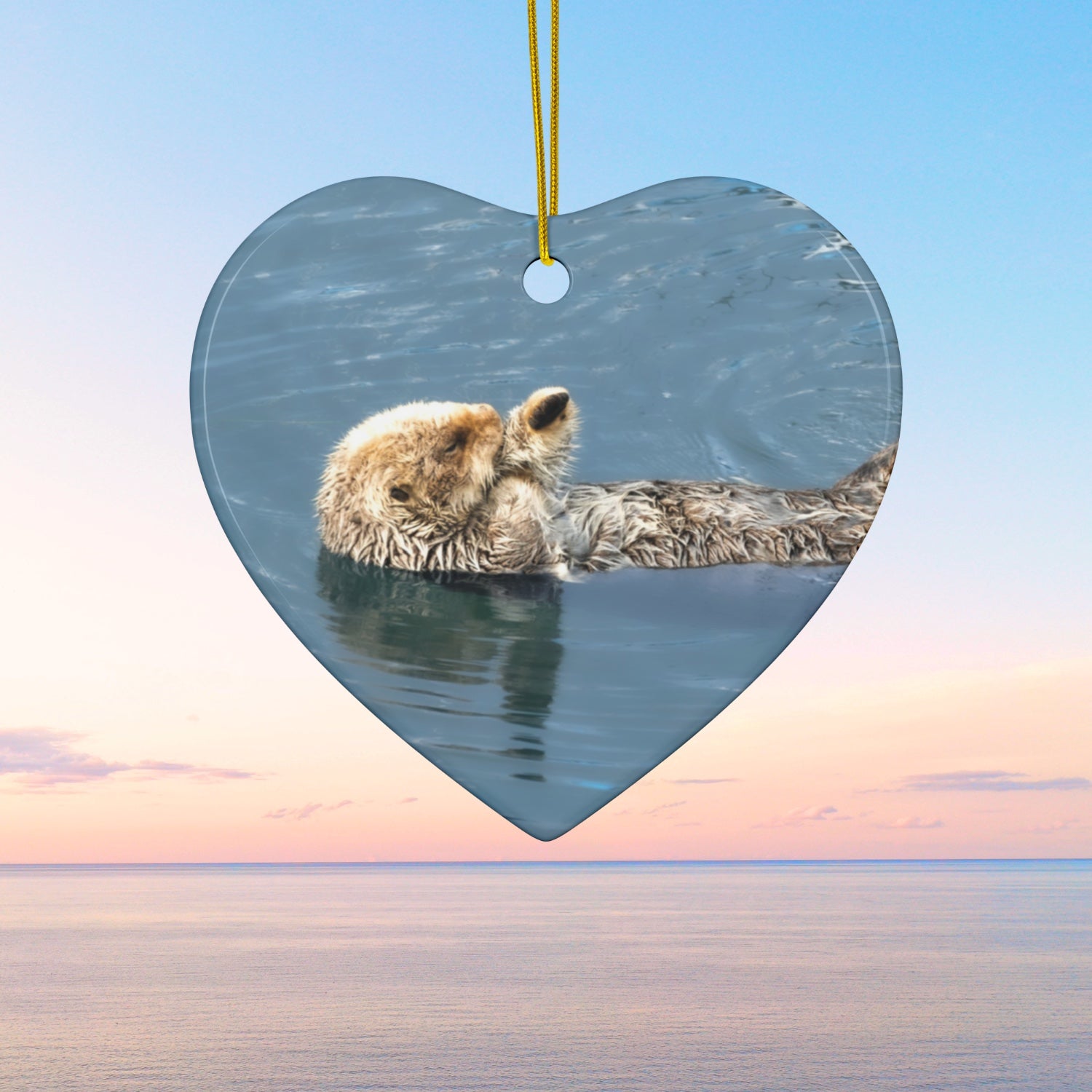 Heart-shaped ornament featuring a professional photograph of a sea otter floating on its back in the blue waters of the Pacific Ocean