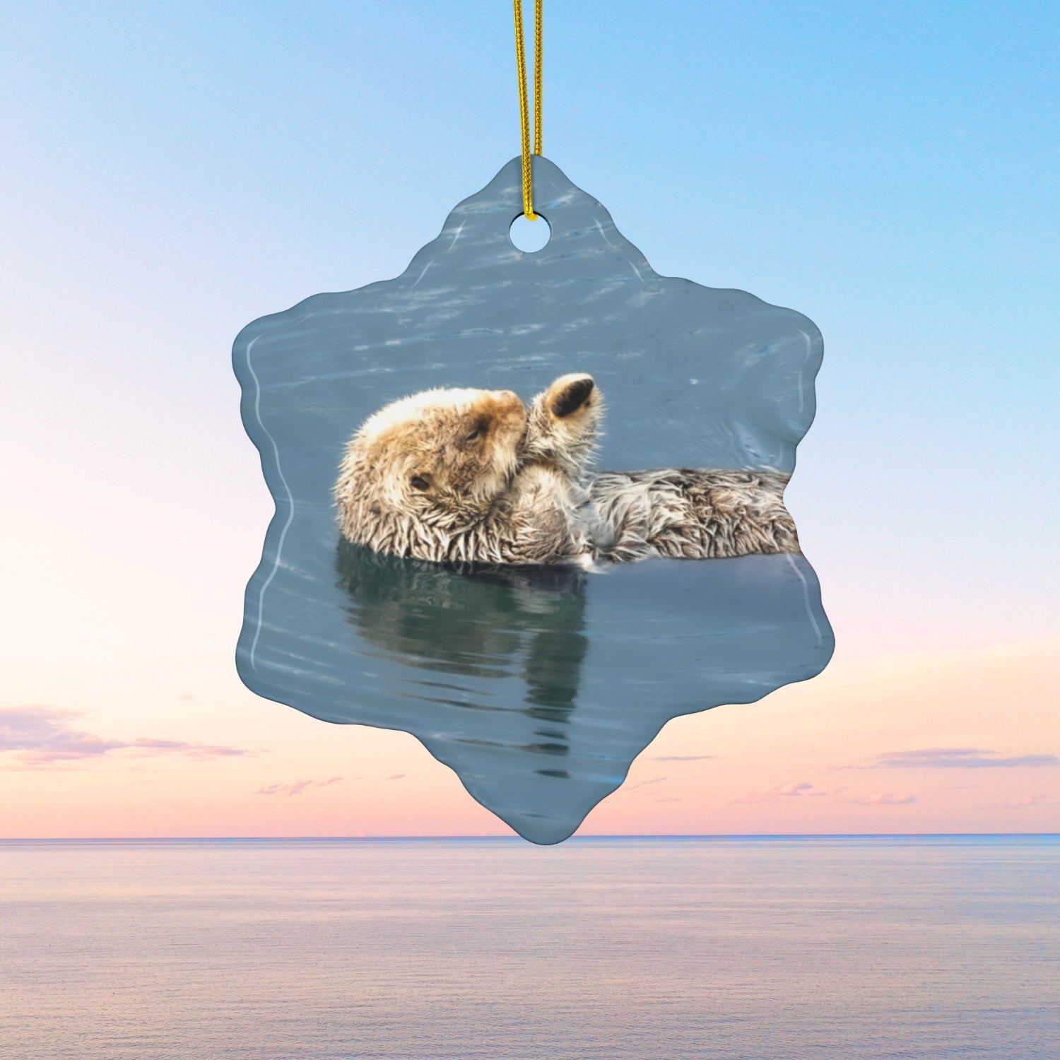Ceramic holiday ornament featuring a professional photograph of a sea otter floating on its back in the blue waters of the Pacific Ocean