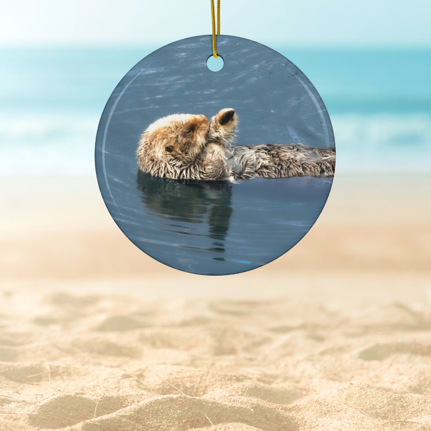Ceramic holiday ornament featuring a professional photograph of a sea otter floating on its back in the blue waters of the Pacific Ocean
