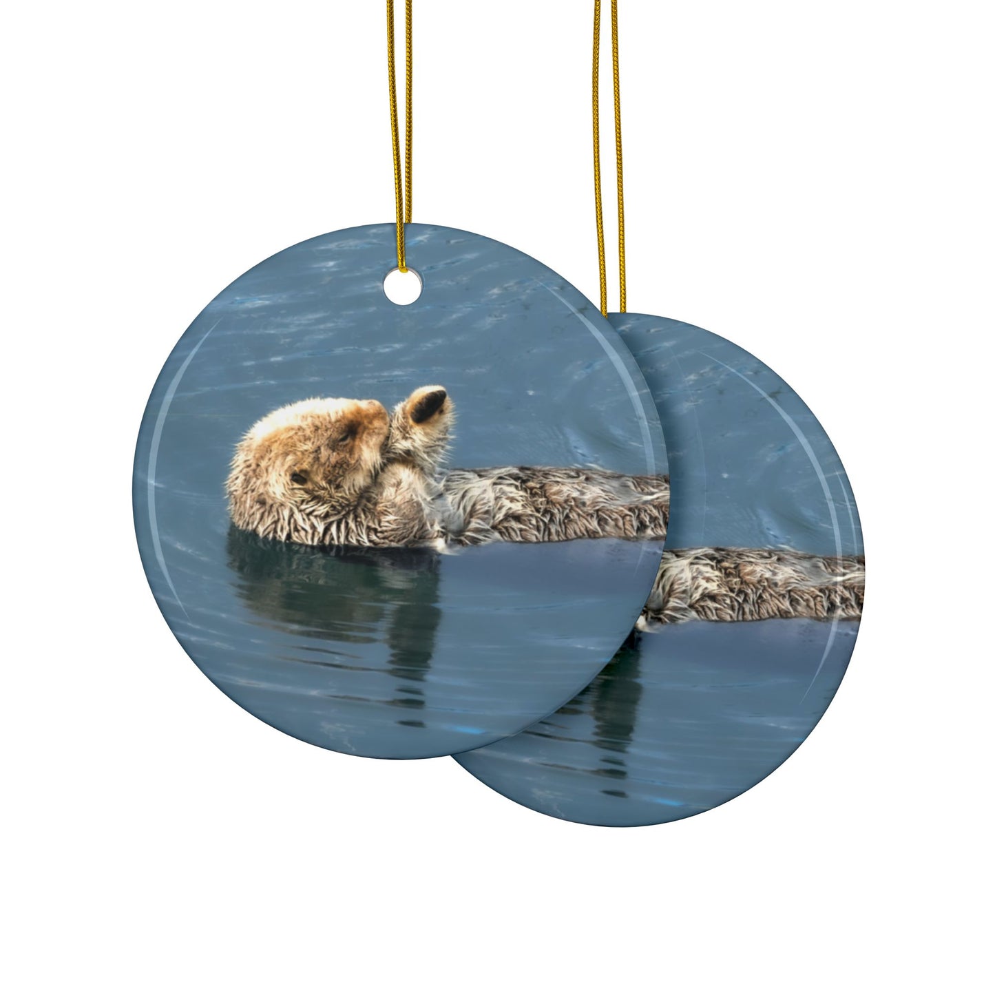 The front and back side of a ceramic holiday ornament featuring a professional photograph of a sea otter floating on its back in the blue waters of the Pacific Ocean