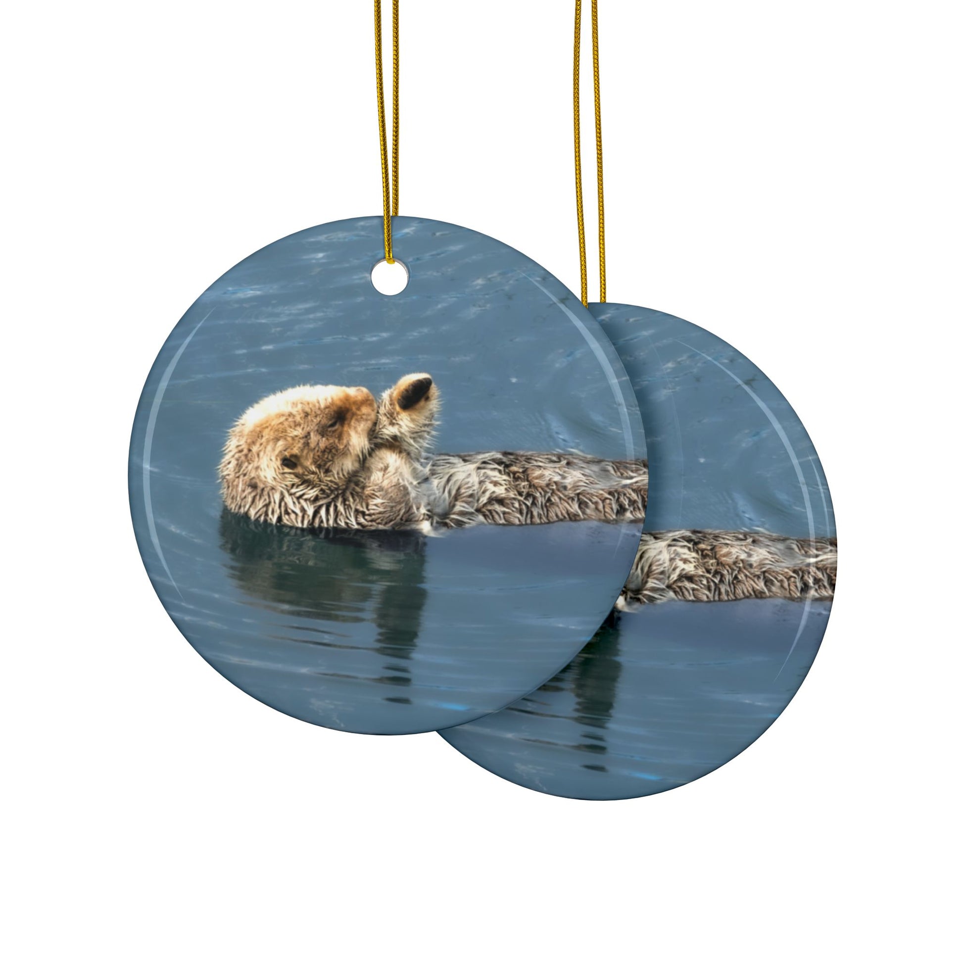 The front and back side of a ceramic holiday ornament featuring a professional photograph of a sea otter floating on its back in the blue waters of the Pacific Ocean