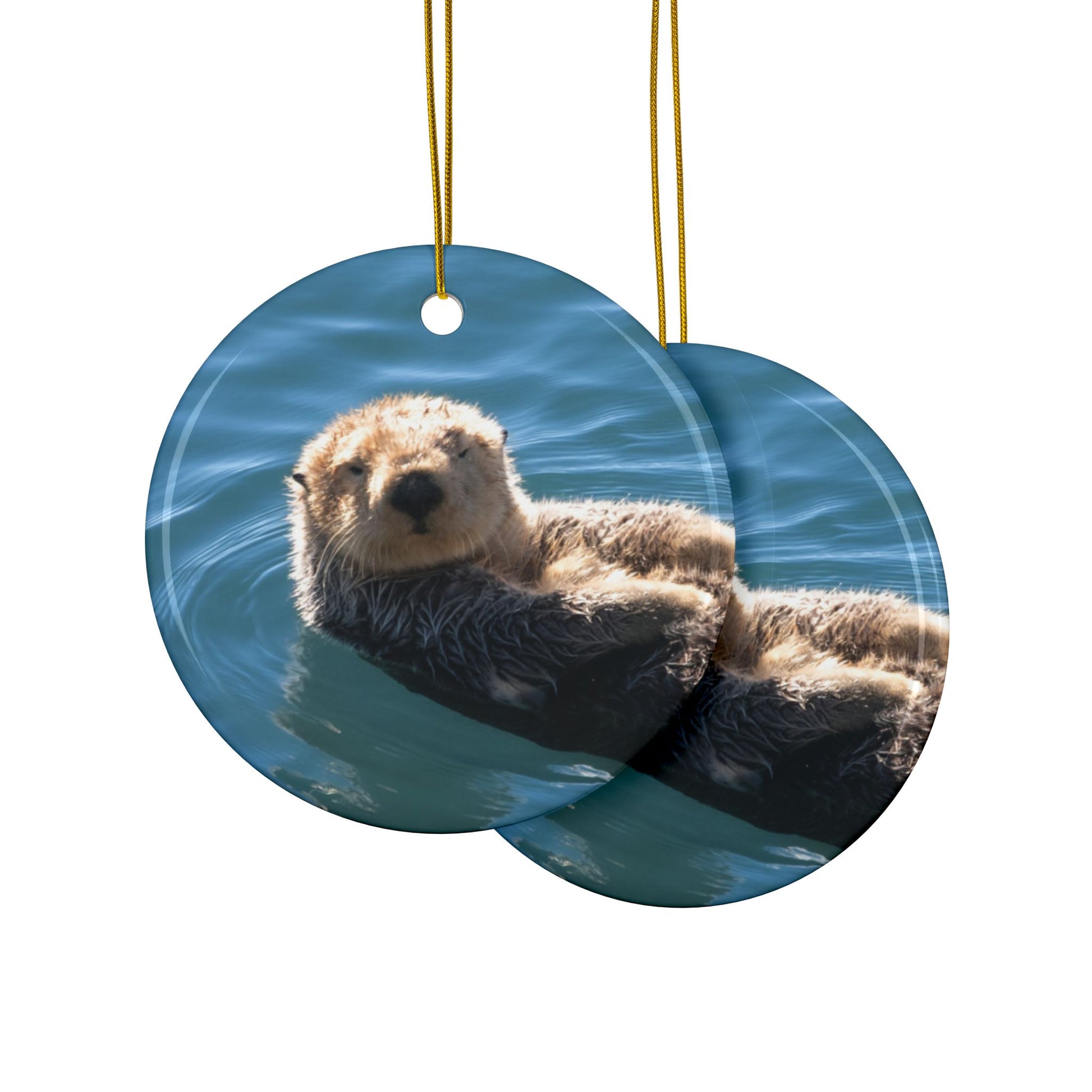 Front and back side of a ceramic Christmas ornament featuring a close-up photograph of a sea otter floating in the calm, blue waters of Morro Bay with golden light on its fur.
