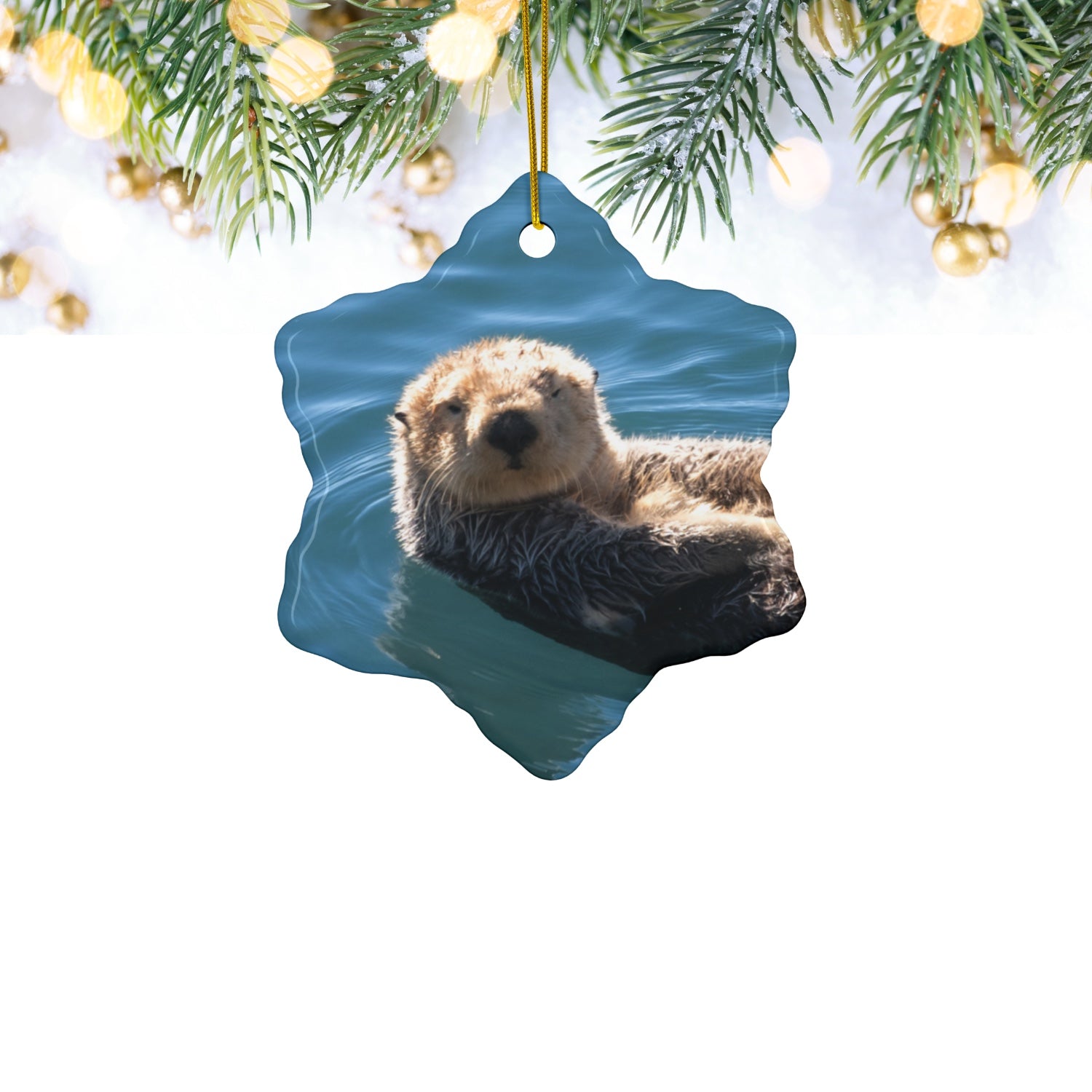 Ceramic Christmas ornament featuring a close-up photograph of a sea otter floating in the calm, blue waters of Morro Bay with golden light on its fur, hanging from Christmas tree.