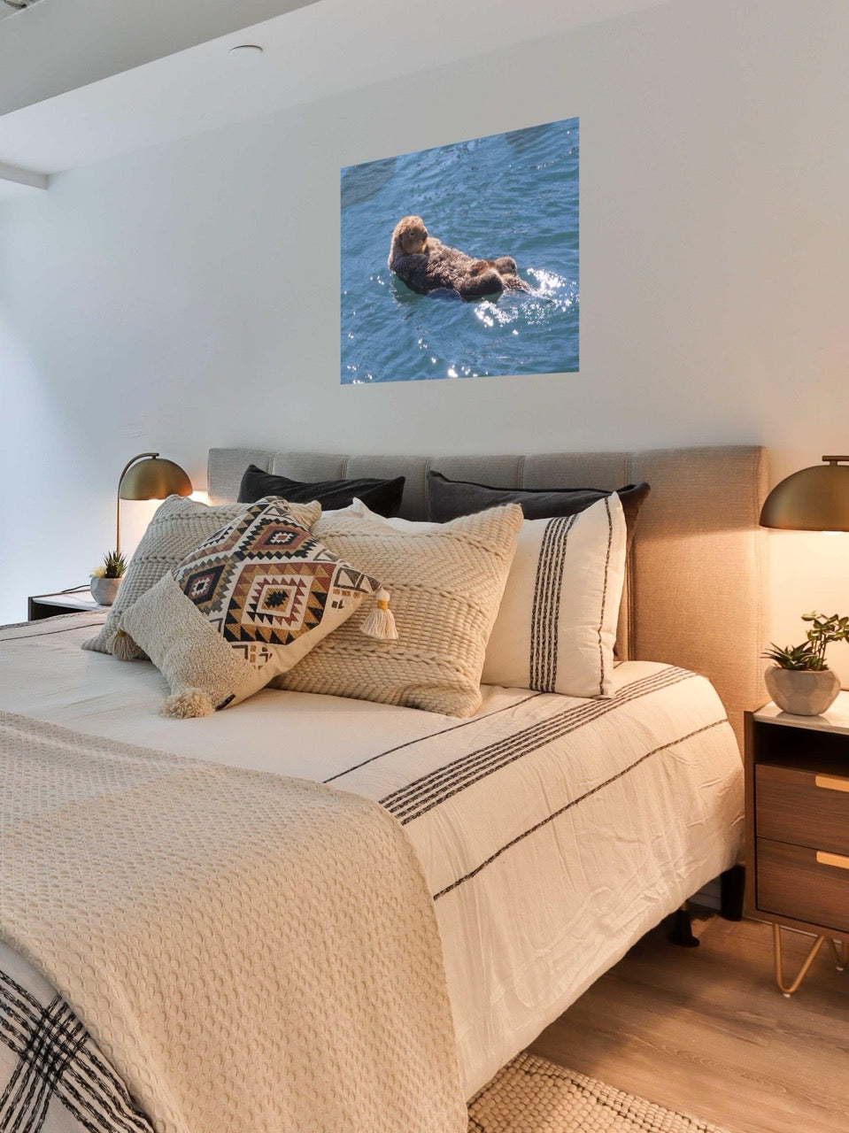 Bedroom with a bed featuring patterned pillows, a lamp on each side, and a wall art of a sea otter in water.