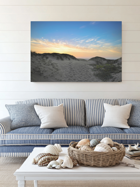 Living room with a couch, coffee table, and a canvas print of a beach sunset over the sand dunes.