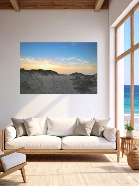 Living room with a canvas print of a beach sunset over the sand dunes, white sofa, and wooden floor.