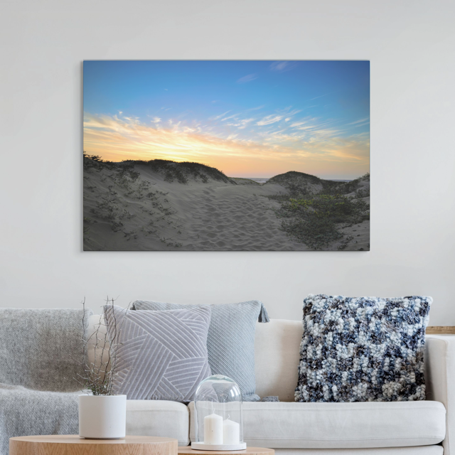 Sofa with decorative pillows and a canvas print of a beach sunset over the sand dunes.