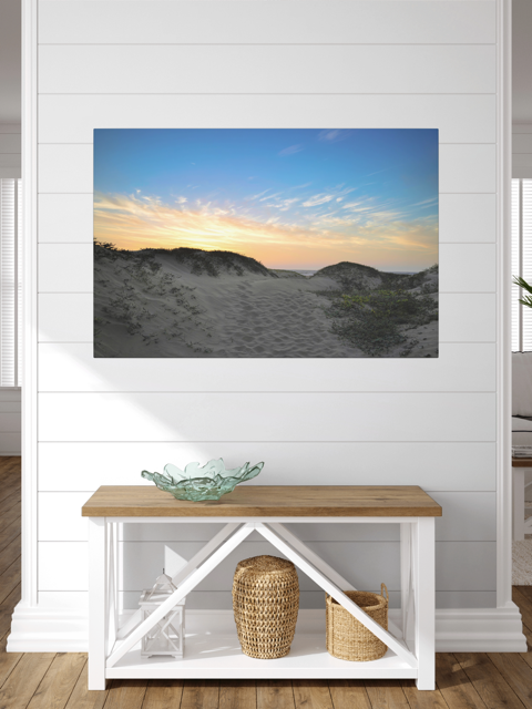 Canvas print of a beach sunset over the sand dunes in a room with a wooden bench and decorative items.
