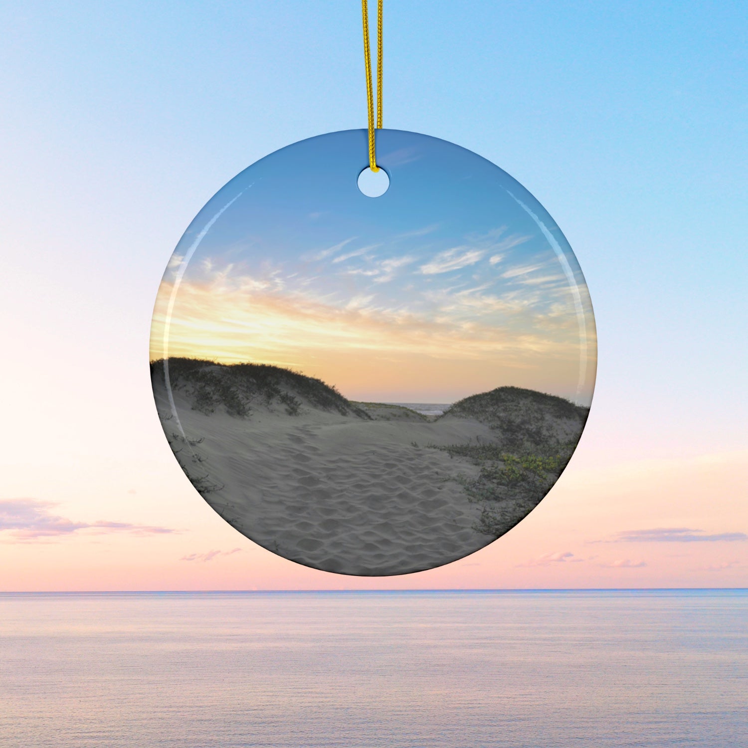 Ceramic holiday ornament featuring a landscape photograph of a California beach at sunset with rolling sand dunes, footprints, and gold-streaked clouds.