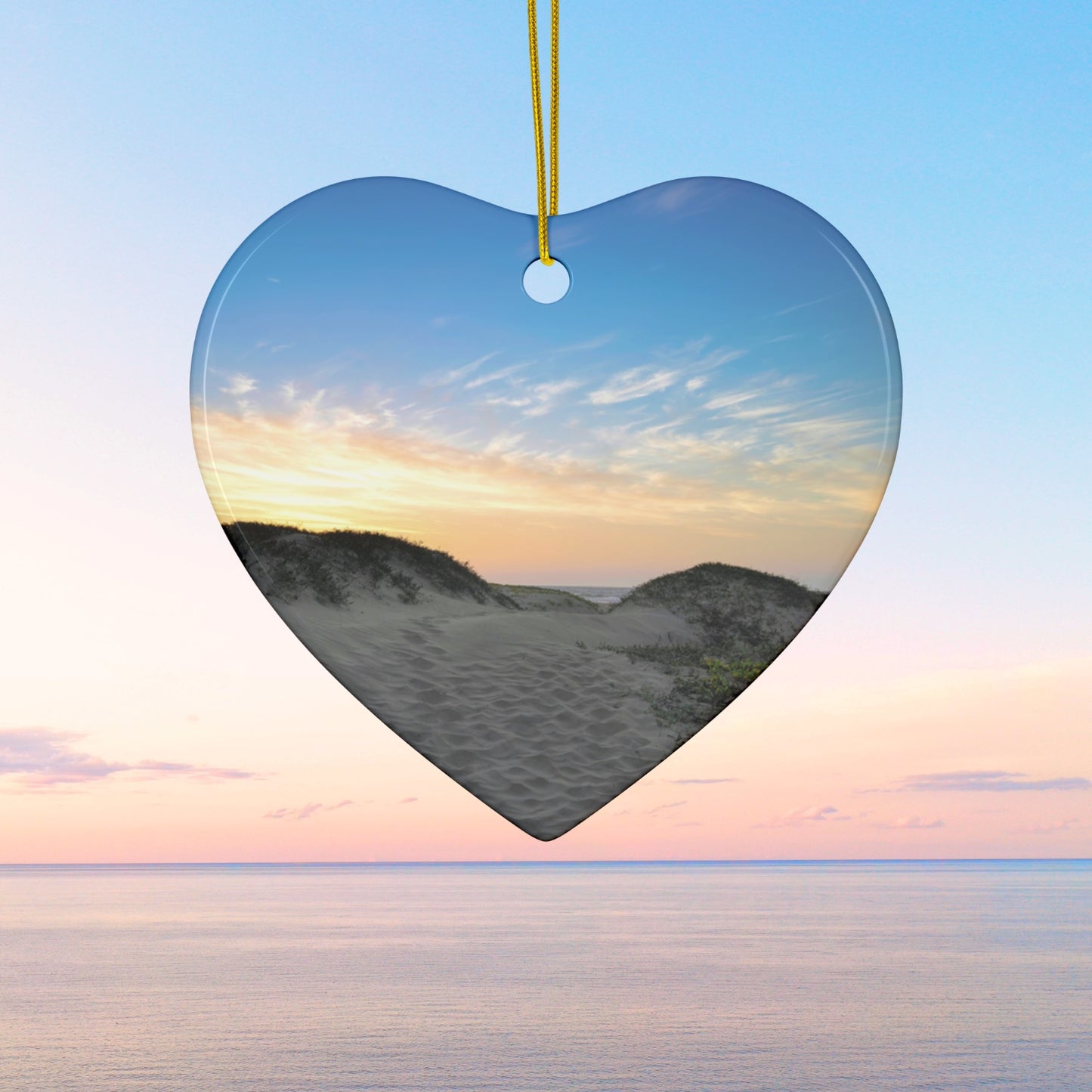 Heart-shaped ceramic holiday ornament featuring a landscape photograph of a California beach at sunset with rolling sand dunes, footprints, and gold-streaked clouds.