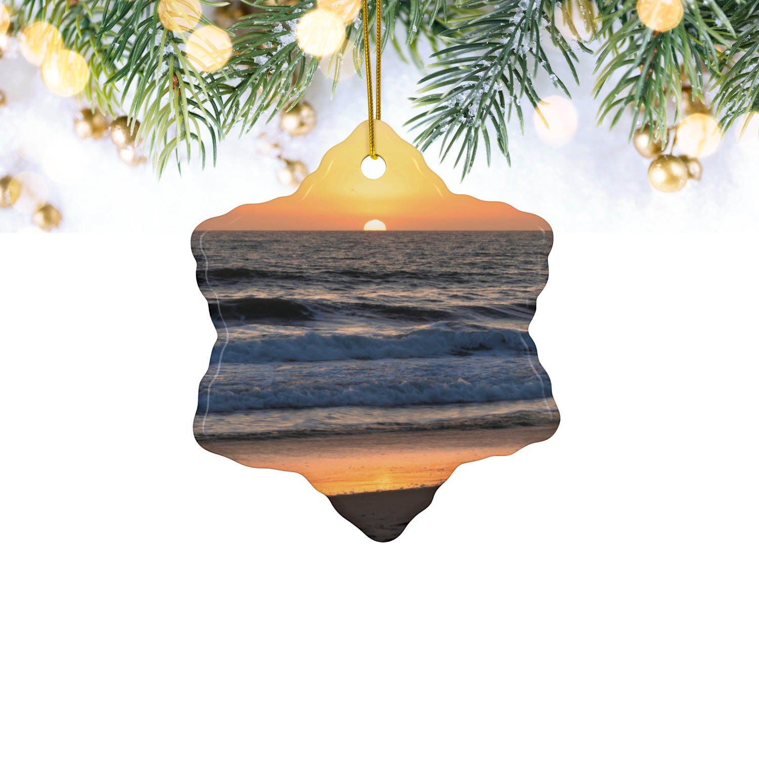 Ceramic Christmas ornament featuring a photograph of a vibrant amber and gold sunset over the Pacific Ocean with waves rolling toward the shore, hanging from Christmas tree.